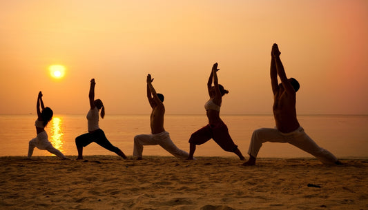 Imagen de 5 personas haciendo yoga en la playa con un atardecer de fondo